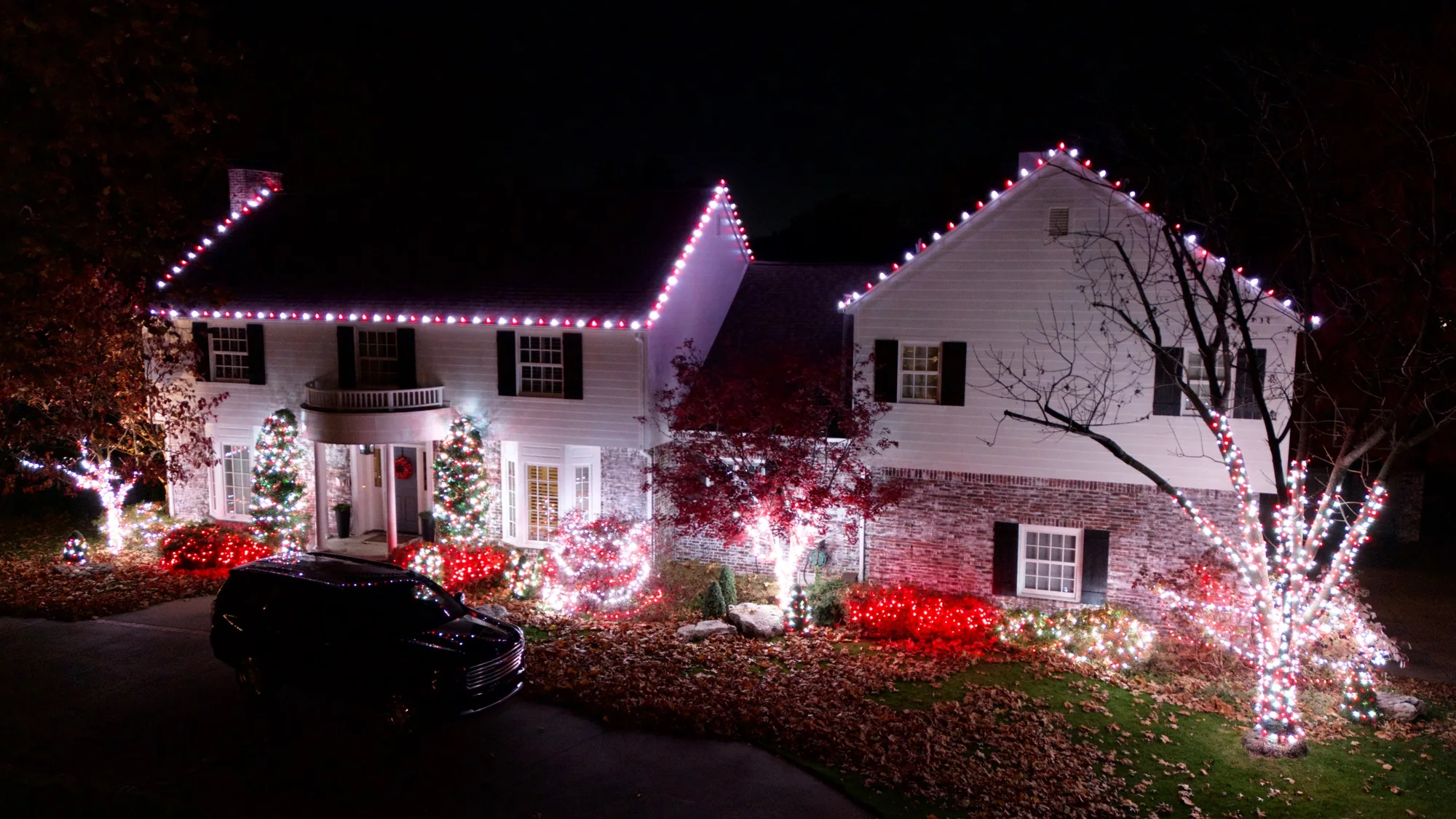 Red and white roofline over wrapped shrubs. Christmas Lighting by LIT Outdoor Lighting in Tulsa.