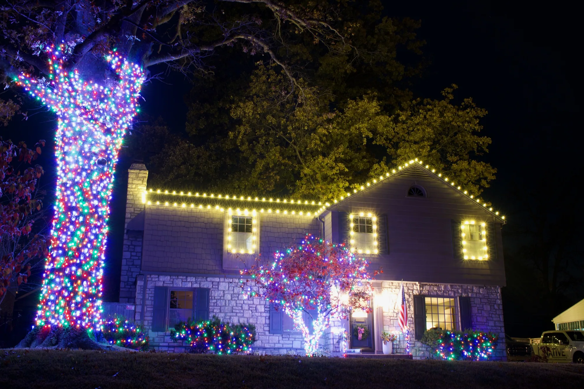 An oak wrapped multicolour by a stone front. Christmas Lighting by LIT Outdoor Lighting in Tulsa.