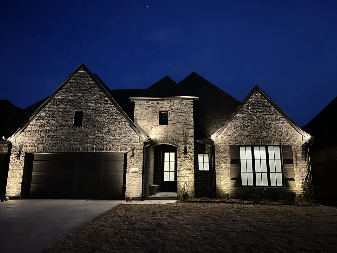 Dark stone facade grazed from the ground. Landscape Lighting by LIT Outdoor Lighting in Tulsa.